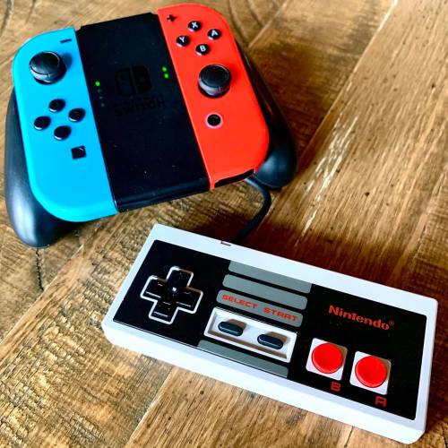 A Nintendo Switch controller in blue and red next to a classic NES controller on a wooden surface.