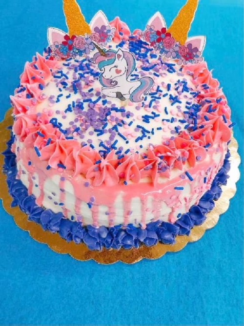 A colorful unicorn-themed cake with pink and blue frosting, topped with sprinkles and decorative unicorn horns.