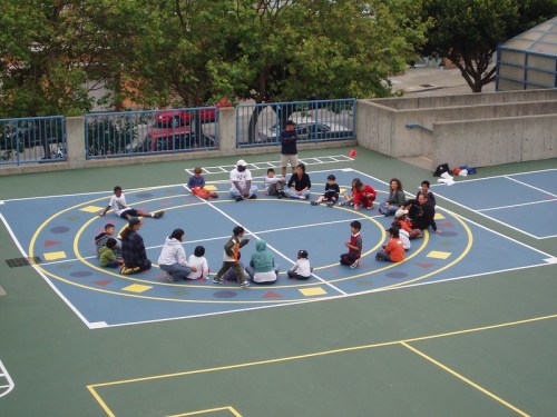 A group of children and adults sitting in a circle on a colorful playground, engaged in an activity.