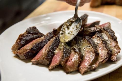 Sliced steak on a plate, being drizzled with a rich sauce.