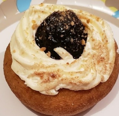 A frosted donut topped with a dark filling and sprinkled with crushed nuts on a paper plate.