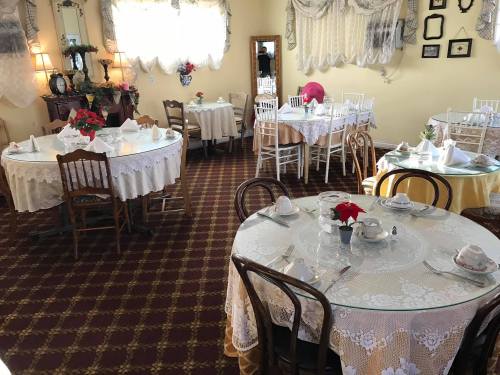 Cozy dining room with elegantly set tables, lace tablecloths, and floral centerpieces in a warm, inviting atmosphere.