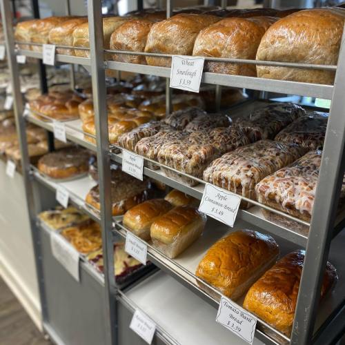 A display of various freshly baked breads on metal shelves, including loaves and rolls, in a bakery setting.