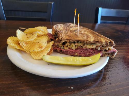 A plate with a sliced sandwich filled with meat and cheese, served with potato chips and a pickle on the side.