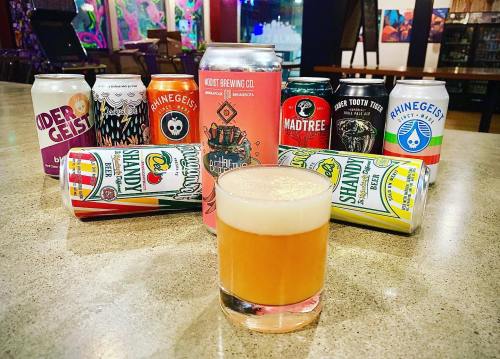 A glass of beer in front of various colorful craft beer cans arranged on a table.