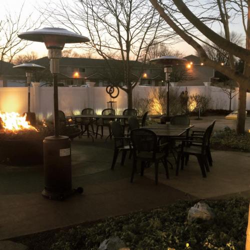 A cozy outdoor seating area with a fire pit and patio heaters, surrounded by trees at dusk.