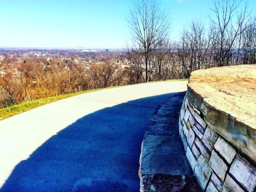 A winding path leads to a scenic overlook with bare trees and a distant view of the landscape under a clear blue sky.