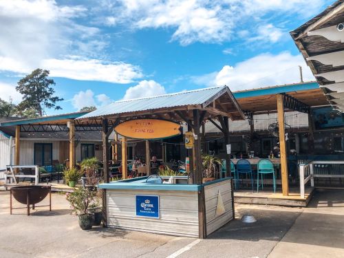 A colorful outdoor dining area with tables, chairs, and a sign reading "Welcome to Tasty Fish" under a blue sky.