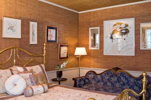 Cozy bedroom featuring a brass bed, floral bedding, a blue sofa, and art on textured brown walls.