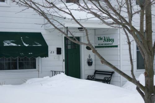 A snowy entrance to a bed and breakfast called "The Abbey," featuring a green awning and a bench.