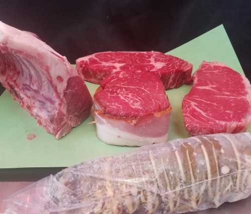 Assorted cuts of raw meat, including ribeye and bacon-wrapped steak, displayed on green paper.