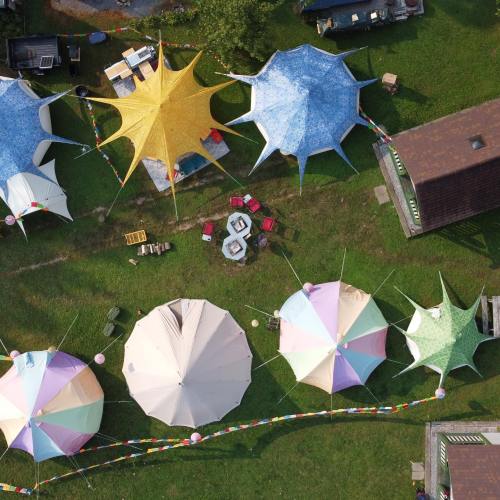 Aerial view of colorful tents and seating arrangements in a grassy area, with decorative flags and a cozy atmosphere.
