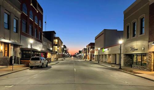 A quiet downtown street at dusk, lined with shops and streetlights, under a gradient sky transitioning to night.