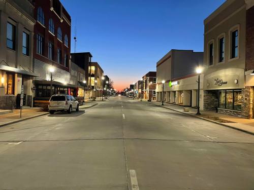 A quiet street at dusk, lined with buildings and streetlights, showcasing a gradient sky transitioning to night.