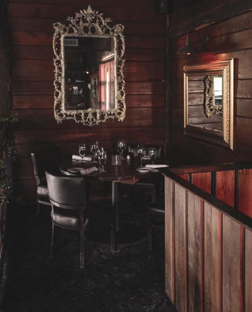 Cozy restaurant corner with dark wood walls, elegant mirrors, and a table set for dining.