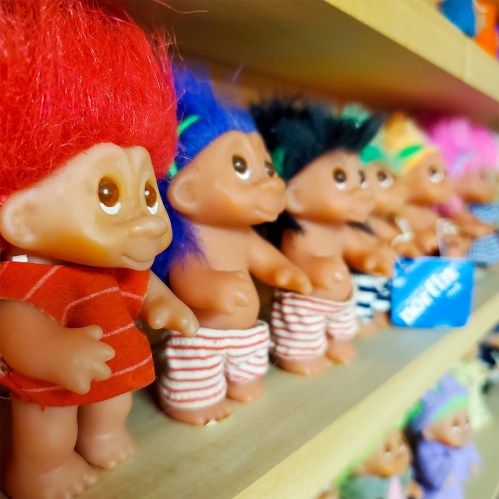 A colorful display of troll dolls with various hairstyles and outfits on a wooden shelf.