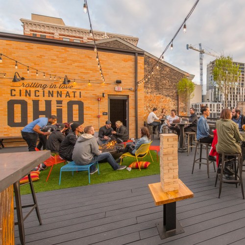 A rooftop gathering in Cincinnati with people socializing, sitting on colorful chairs, and enjoying the outdoor space.