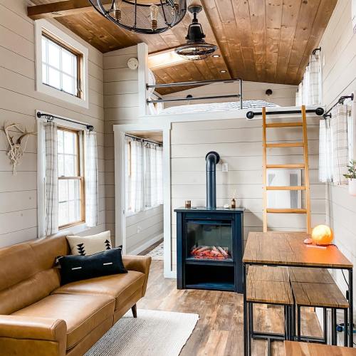 Cozy interior of a small cabin with a loft bed, wooden accents, a sofa, and a modern electric fireplace.