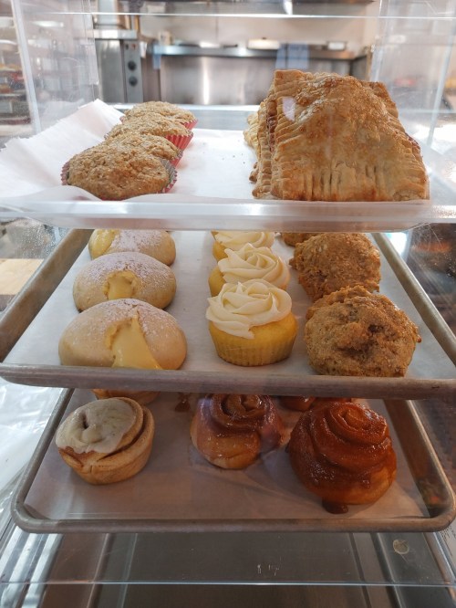 A display case with assorted baked goods: muffins, pastries, cupcakes, cookies, and cinnamon rolls.