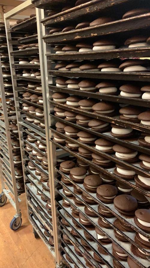 Rows of trays filled with chocolate whoopie pies, stacked high in a bakery setting.