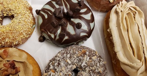 A variety of colorful donuts, including chocolate, caramel, and nut toppings, arranged on a white tray.