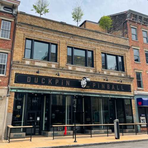 Exterior of Duckpin Pinball, a brick building with large windows and greenery on the roof, in an urban setting.