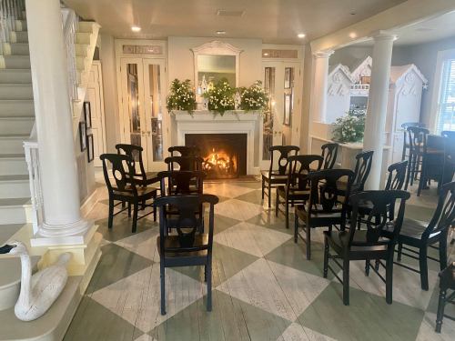 A cozy room with a fireplace, surrounded by black chairs and decorative plants, featuring a patterned floor and staircase.