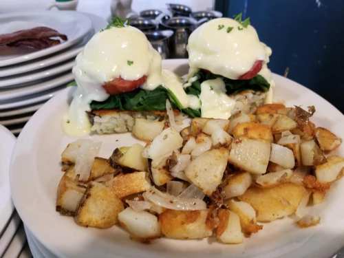 Two eggs Benedict on a bed of spinach and rice, served with a side of crispy diced potatoes.