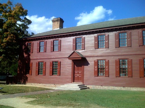 A red wooden building with multiple windows and a central door, set against a blue sky with scattered clouds.