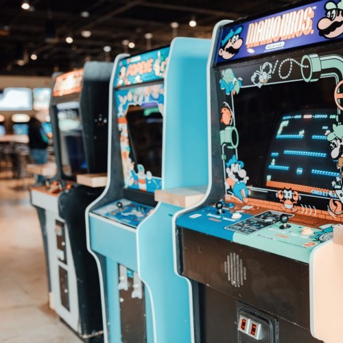 A row of vintage arcade machines in a gaming venue, featuring colorful screens and classic designs.