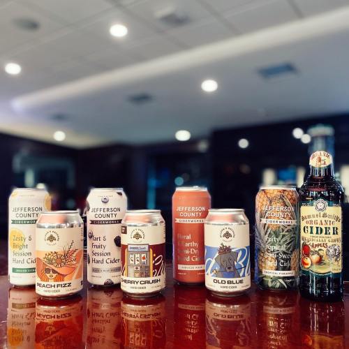 A variety of cider cans displayed on a table, featuring flavors like Beach Fizz, Berry Crush, and Old Blue.
