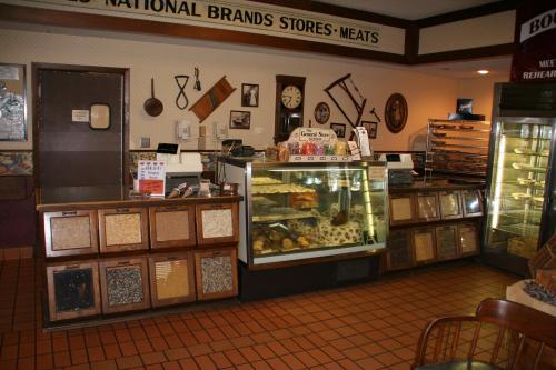 A cozy deli interior featuring a display case of baked goods, wooden cabinets, and vintage decor on the walls.