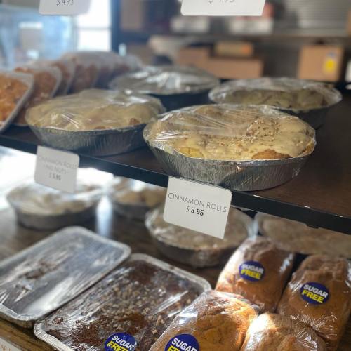 Baked goods displayed in a bakery, including cinnamon rolls and various desserts, all covered with plastic wrap.