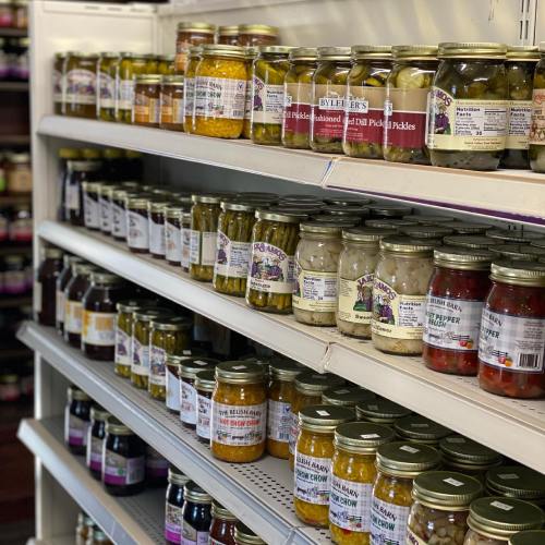 Shelves filled with various jars of pickles and preserves in a store, showcasing colorful labels and different sizes.