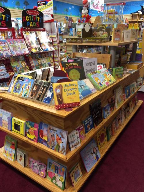 A colorful display of children's books and activity pads on a wooden shelf in a cozy bookstore.