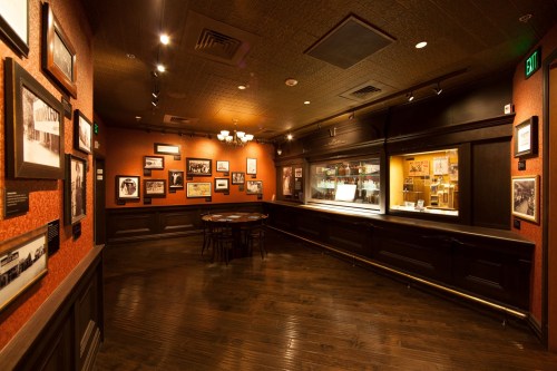 Interior of a dimly lit room with wooden floors, featuring framed photos on the walls and a display case.