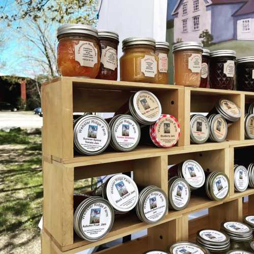 A wooden display featuring jars of various jams and preserves, labeled and arranged neatly in rows.