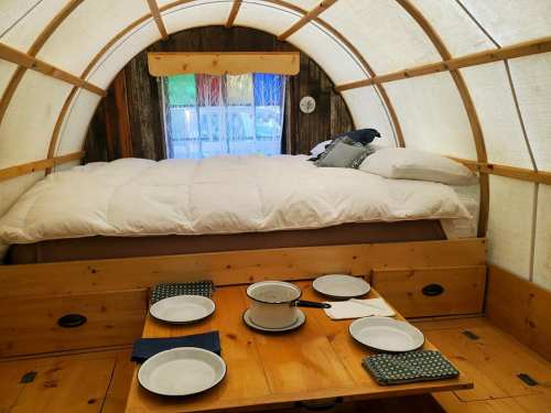 Cozy interior of a glamping tent featuring a bed and a dining table set with plates.