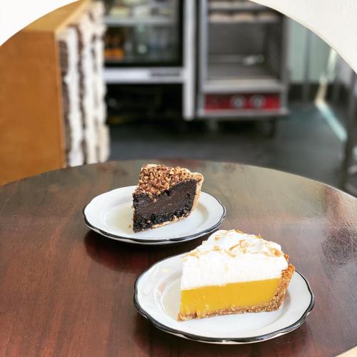 A slice of chocolate cake and a slice of lemon pie on white plates, set on a wooden table.
