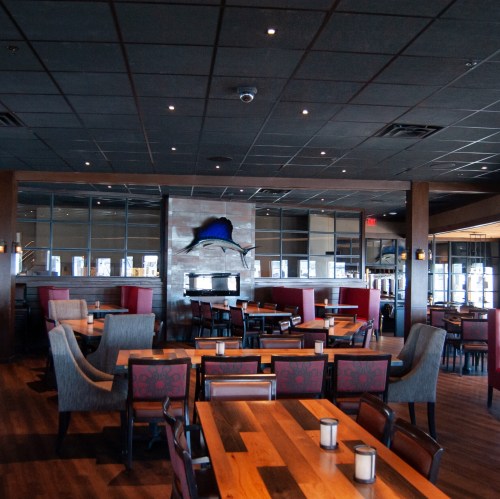 Interior of a modern restaurant featuring wooden tables, upholstered chairs, and a large mural on the wall.