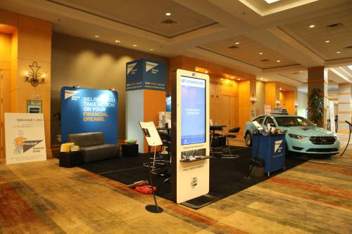 A trade show booth featuring a sleek car, informational displays, and seating in a well-lit conference space.