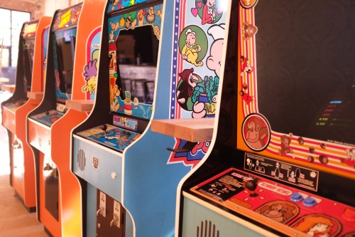 A row of colorful vintage arcade game machines with various cartoon graphics and designs.