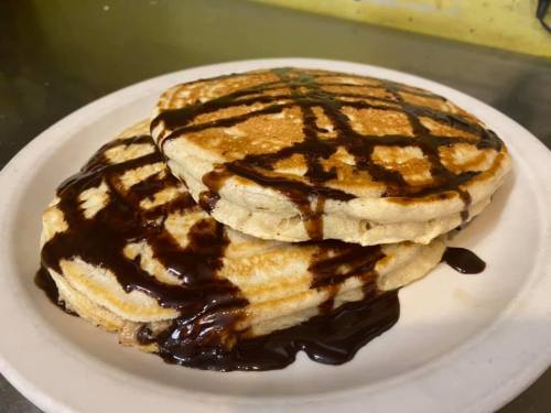 Three fluffy pancakes drizzled with rich chocolate syrup on a white plate.