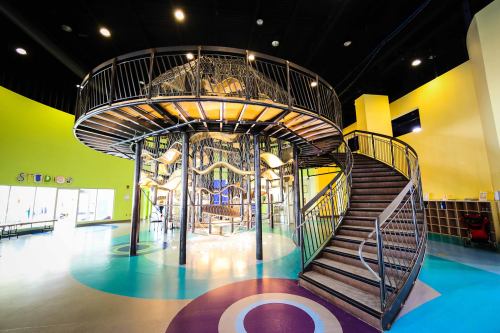 A colorful indoor play area featuring a multi-level climbing structure and a spiral staircase.