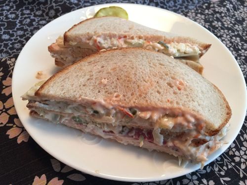 A plate with two halves of a sandwich filled with creamy salad and served with a pickle on the side.