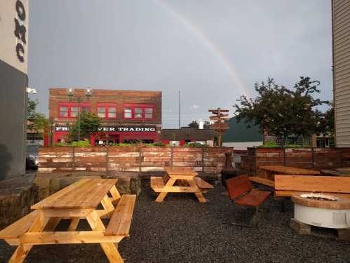 Outdoor seating area with wooden picnic tables, surrounded by greenery, and a rainbow in the sky after a rainstorm.