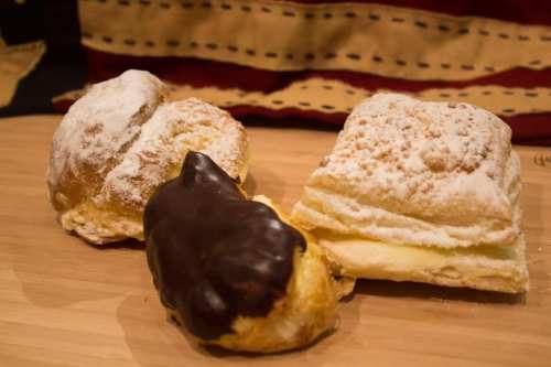 Three pastries on a wooden surface: two with powdered sugar and one coated in chocolate.