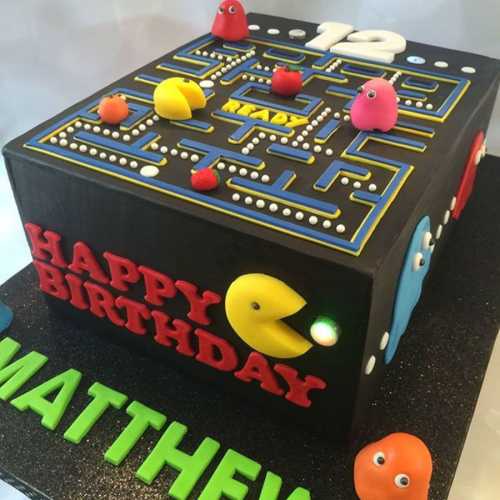 A colorful birthday cake themed like a Pac-Man game, featuring "Happy Birthday Matthew" and game elements on top.