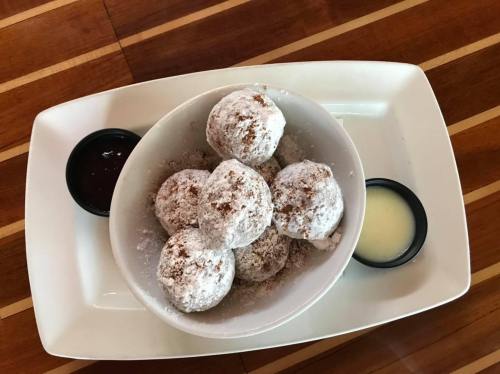 A bowl of powdered sugar-dusted dough balls served with chocolate and cream sauces on the side.