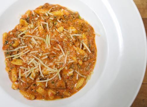 A plate of pasta with a rich tomato sauce, topped with grated cheese and herbs, served on a white dish.
